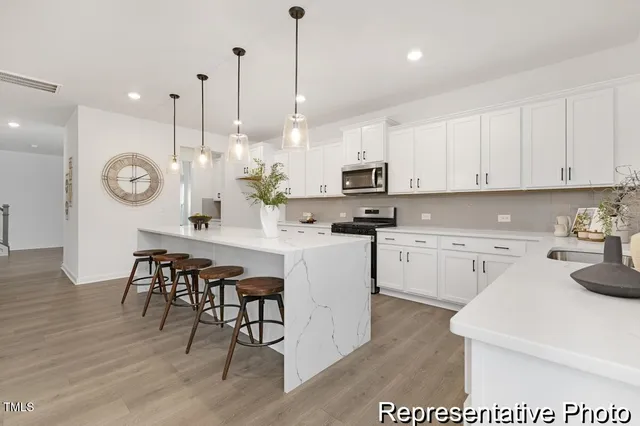 a large white kitchen with kitchen island a large counter space a sink stainless steel appliances and cabinets