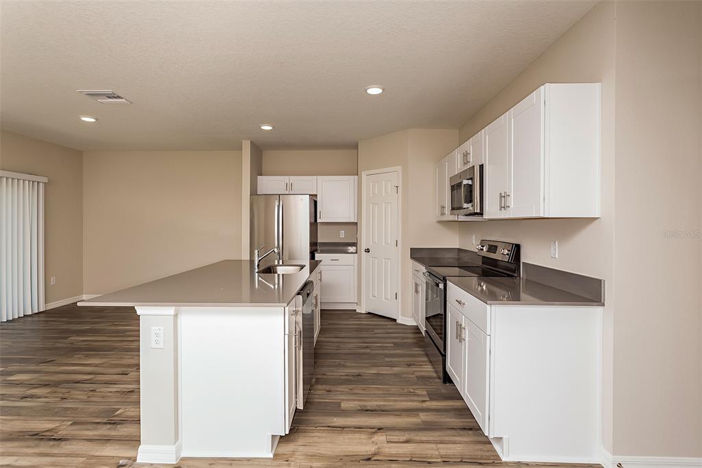 15232 Maude Lndg Loop Wimauma, FL 33598 - Photo 6 of 22 a kitchen with stainless steel appliances granite countertop a refrigerator a stove and a sink with wooden floors