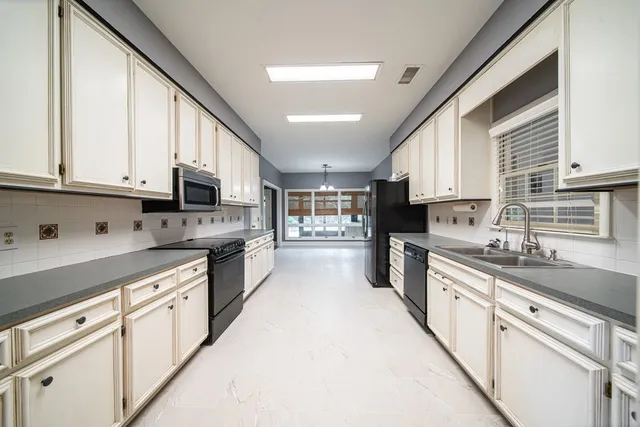 a large kitchen with stainless steel appliances granite countertop a stove a sink a refrigerator and white cabinets