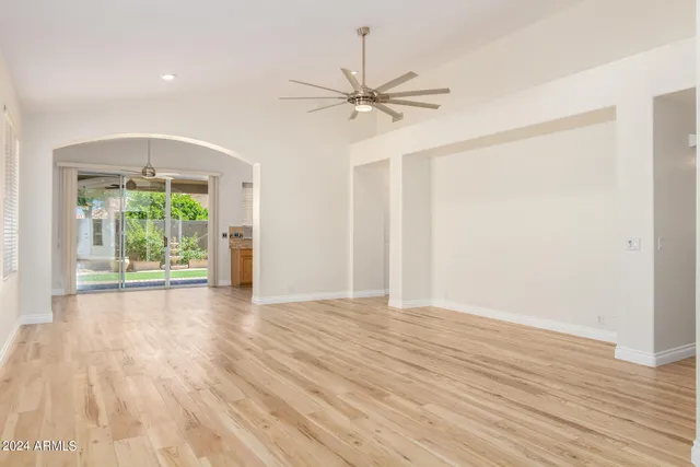 an empty room with wooden floor fan and windows