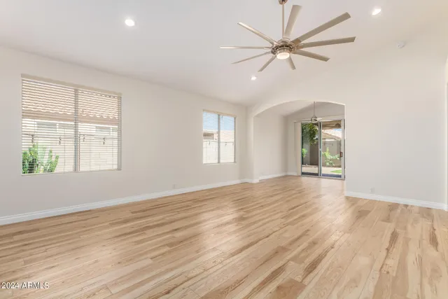 an empty room with wooden floor chandelier fan and windows