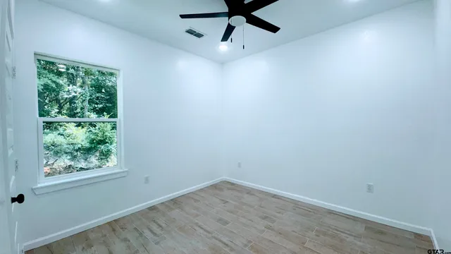 a view of empty room with wooden floor and fan