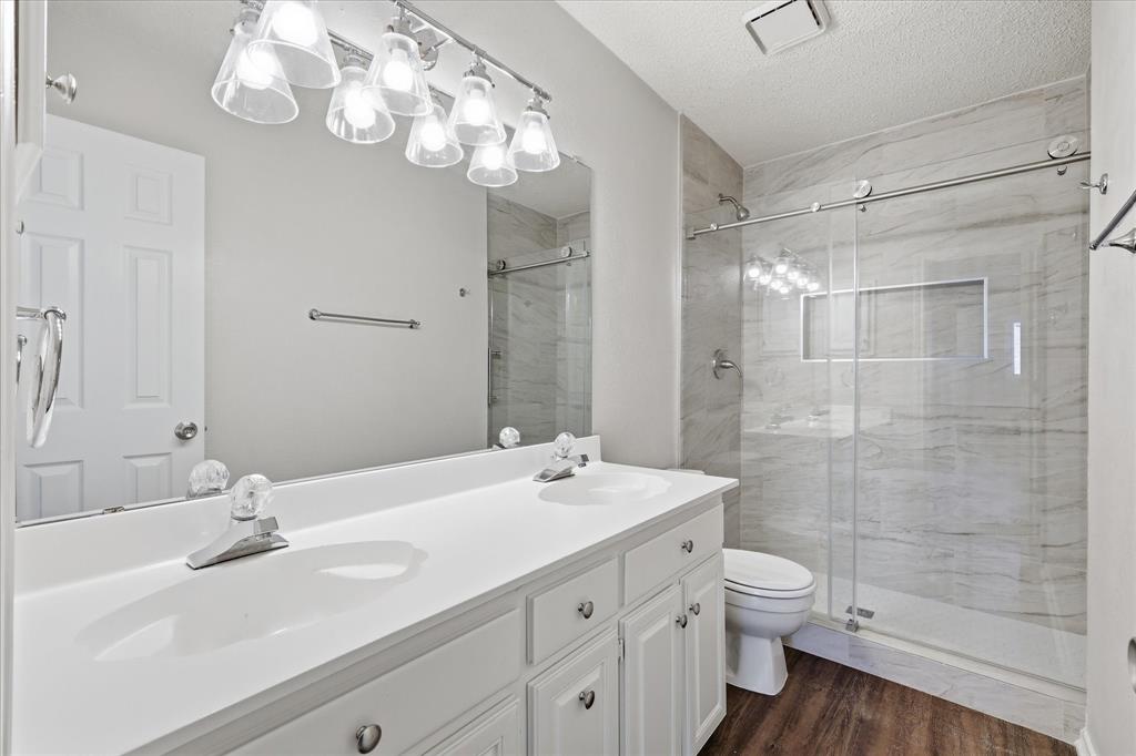 318 Lodge Road Coppell, TX 75019 - Photo 28 of 35 A beautifully updated bath showcases dual sinks and a striking walk-in shower with floor-to-ceiling tile and frameless glass.