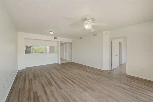 an empty room with wooden floor chandelier fan and windows