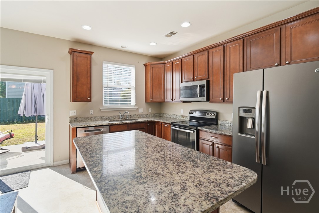 100 Smoke Rise Road Richmond Hill, GA 31324 - Photo 14 of 50 Kitchen with large granite island, stainless steel appliances, wood cabinets, corner sink under window, and sliding glass door leading to the backyard.