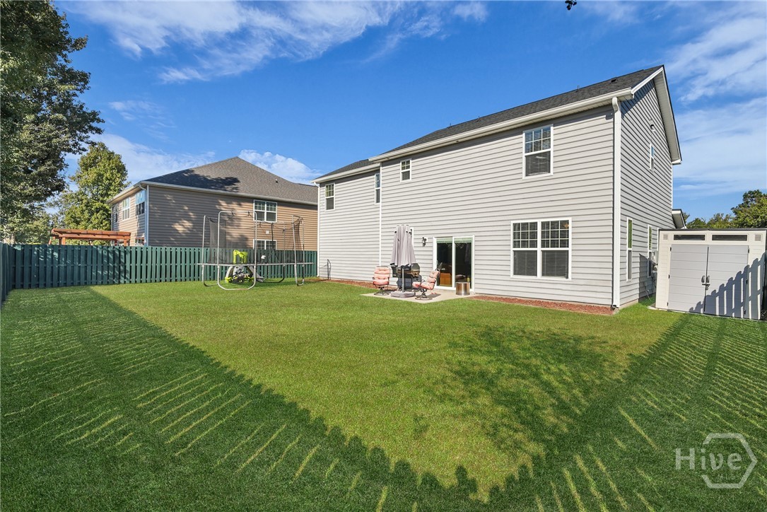 100 Smoke Rise Road Richmond Hill, GA 31324 - Photo 45 of 50 Fenced backyard with a large grassy lawn and rear view of a two-story gray siding home with multiple windows and a sliding glass door.