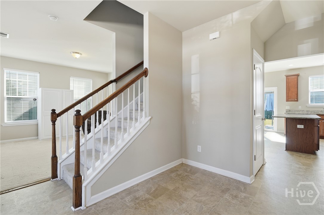 100 Smoke Rise Road Richmond Hill, GA 31324 - Photo 6 of 50 Interior view of a home entryway with tile flooring, a carpeted staircase with wood handrail, neutral wall paint, and an open layout leading to the living room and kitchen with granite countertops.