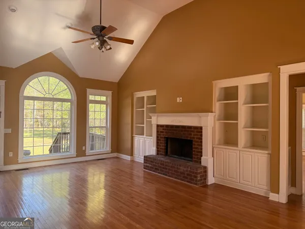 a view of an empty room with wooden floor fireplace and a window