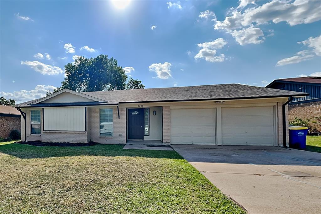Ranch-style home featuring an attached garage, roof with shingles, concrete driveway, a front lawn, and brick siding