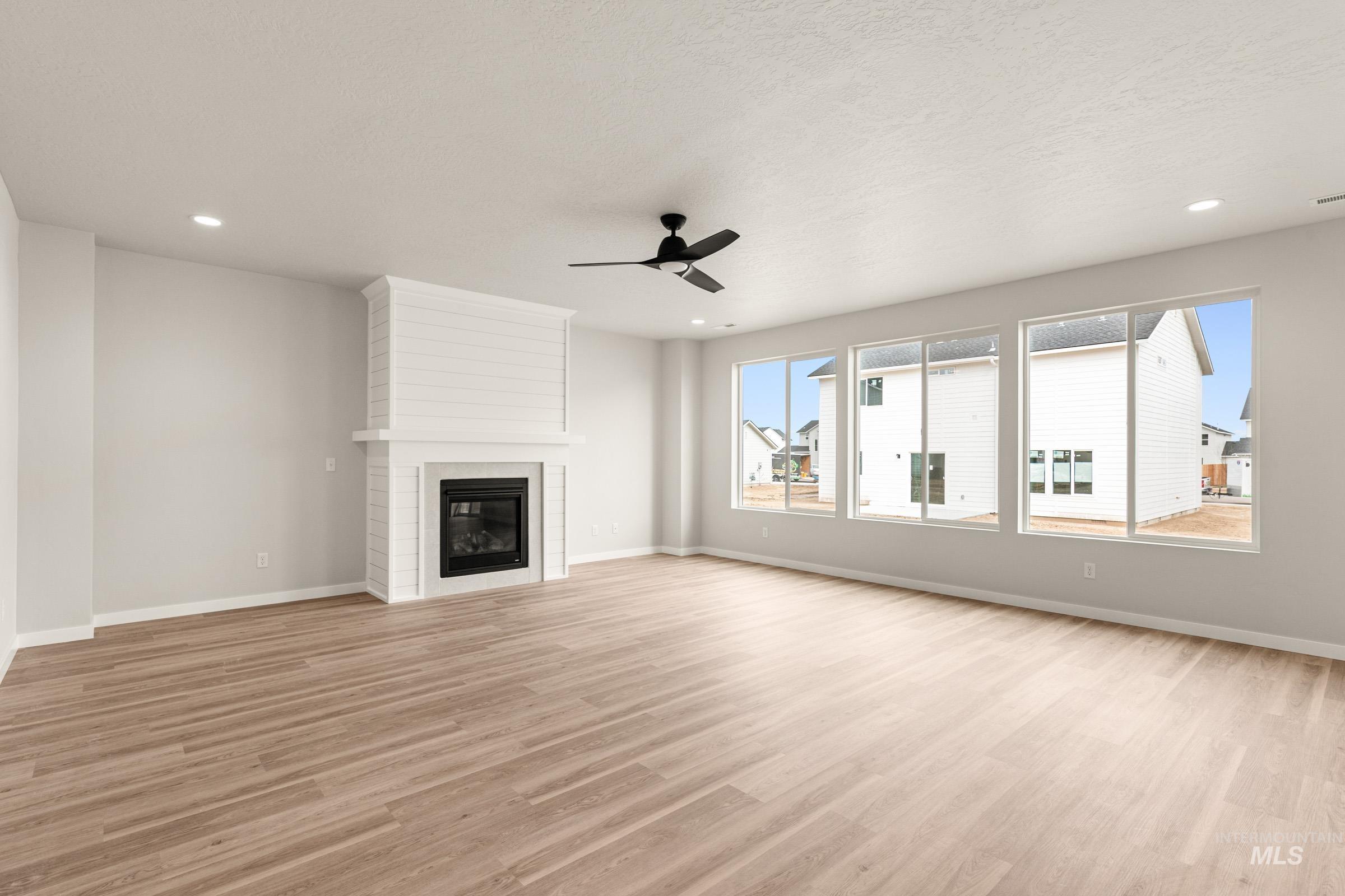 13688 Redway Court Caldwell, ID 83607 - Photo 8 of 26 Unfurnished living room with light wood-style floors, a ceiling fan, a large fireplace, recessed lighting, and a textured ceiling