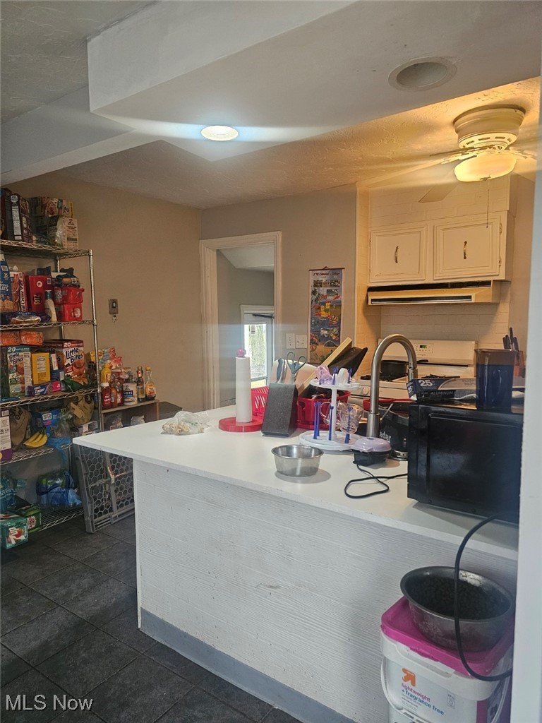 1149 Dorsh Road Cleveland, OH 44121 - Photo 3 of 11 Kitchen with white cabinets, light countertops, white range oven, under cabinet range hood, and dark tile patterned flooring