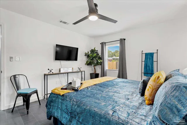 a bedroom with a bed a chair and potted plant on the dresser