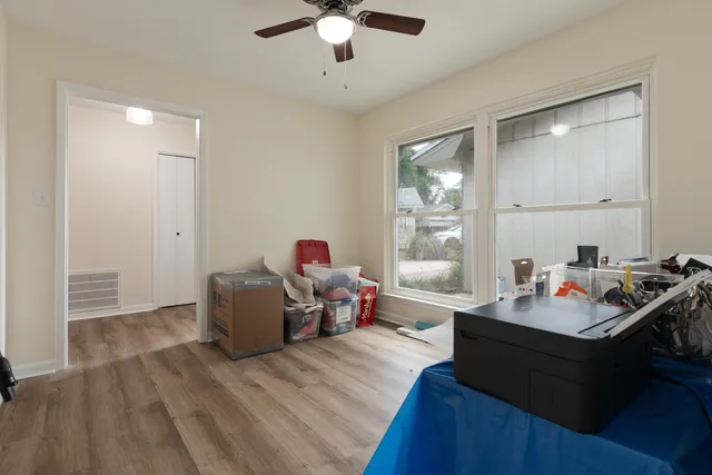 an empty room with wooden floor ceiling fan and windows