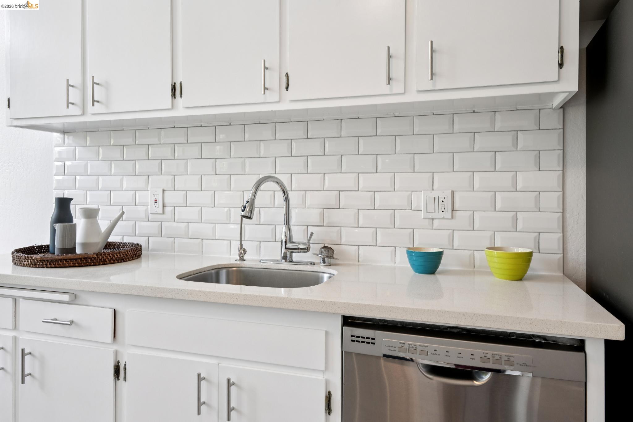 1340 Henry Street Berkeley, CA 94709 - Photo 23 of 52 Kitchen featuring white cabinetry with brushed nickel hardware, white subway tile backsplash, light-toned countertop, stainless steel sink with pull-down faucet, and a stainless steel dishwasher