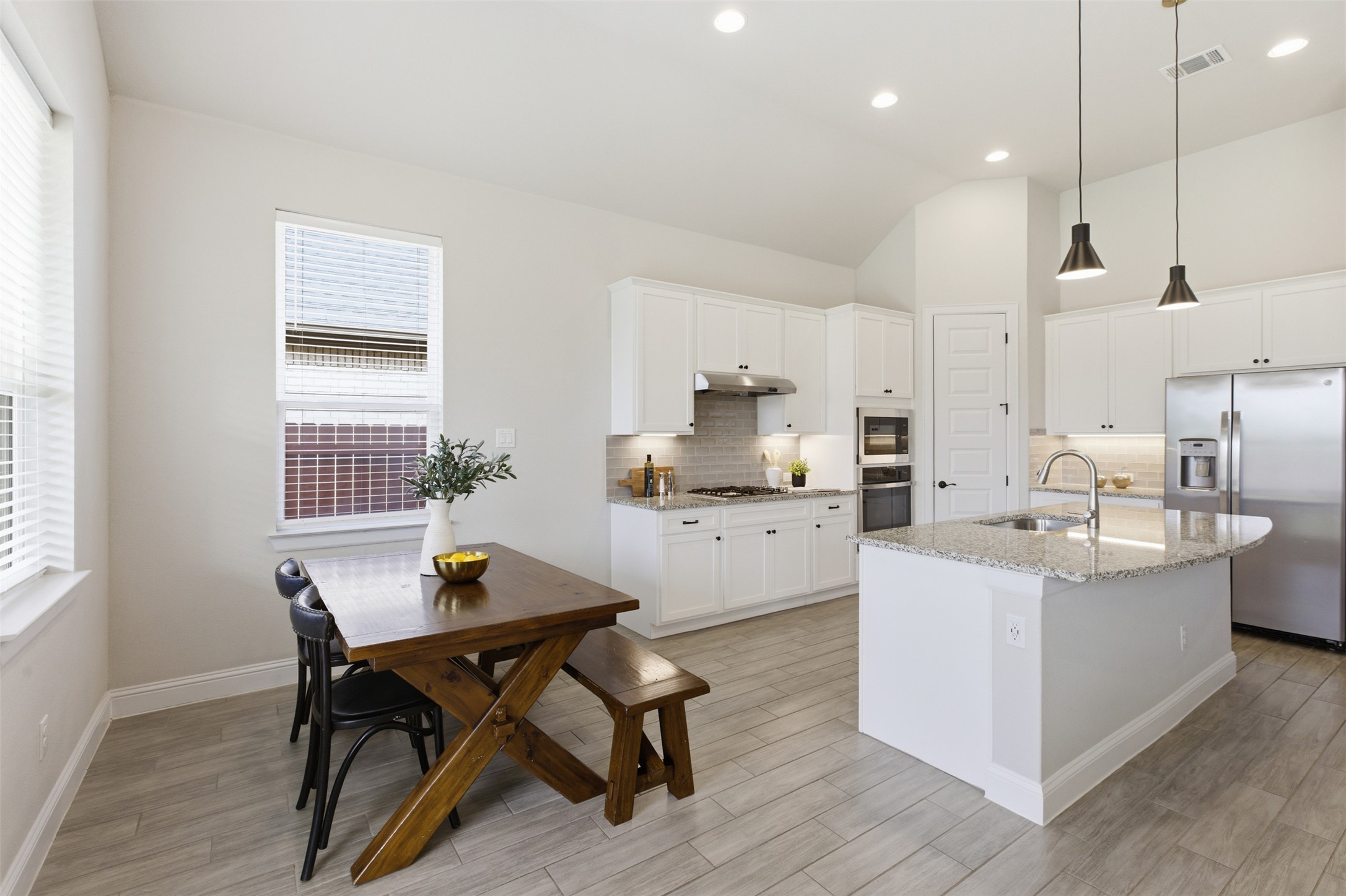 117 Old Trinity Way Georgetown, TX 78628 - Photo 13 of 38 Kitchen featuring stainless steel appliances, light stone counters, decorative backsplash, a center island with sink, and light wood finished floors