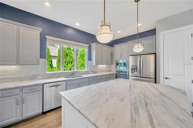 a kitchen with stainless steel appliances granite countertop a refrigerator a sink dishwasher a stove and white countertops with wooden floor