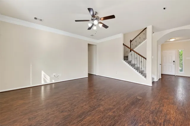 a view of an empty room with wooden floor and a ceiling fan