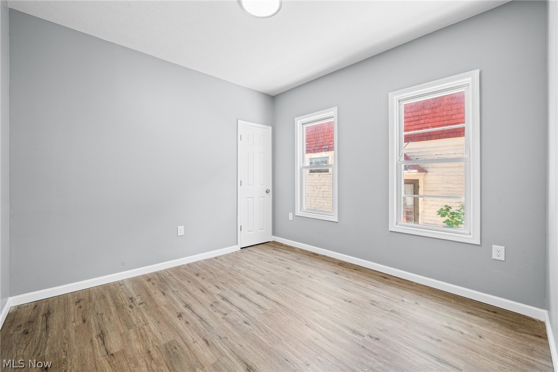 3925 Riverside Avenue Cleveland, OH 44109 - Photo 16 of 48 Spacious room featuring light gray walls, wood-finish flooring, two large windows with white trim, a white paneled door, and a flush mount ceiling light