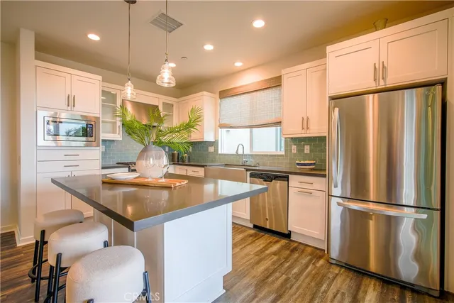 a kitchen with stainless steel appliances granite countertop a refrigerator a sink dishwasher a stove with white cabinets and wooden floor