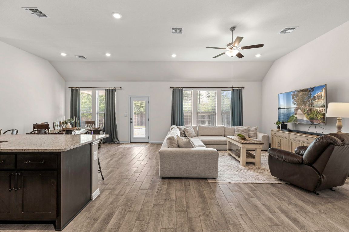232 Silver Pass Kyle, TX 78640 - Photo 13 of 39 Natural light pours through a full wall of windows, highlighting vaulted ceilings and open concept flow. This warm, inviting living area is perfect for movie nights or family gatherings