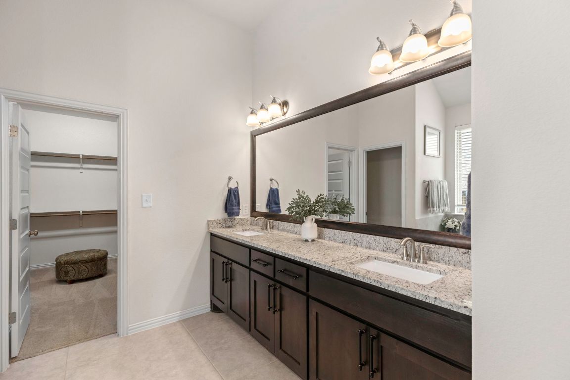 232 Silver Pass Kyle, TX 78640 - Photo 23 of 39 An extended dual sink vanity with granite countertops, framed mirror, and modern lighting gives the primary bath its polished, luxurious vibe