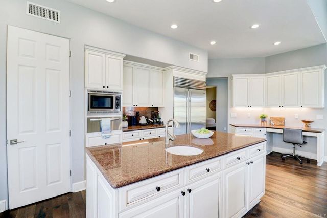a kitchen with stainless steel appliances granite countertop a sink dishwasher and white cabinets with wooden floor