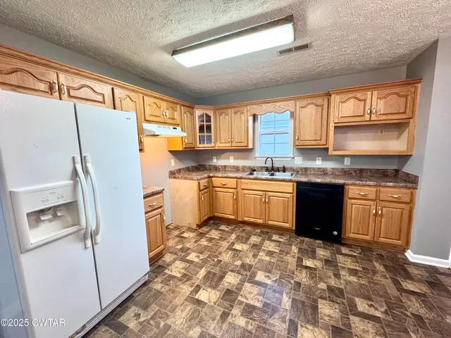 a kitchen with stainless steel appliances granite countertop a refrigerator sink and wooden cabinets