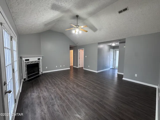 an empty room with wooden floor fireplace and windows