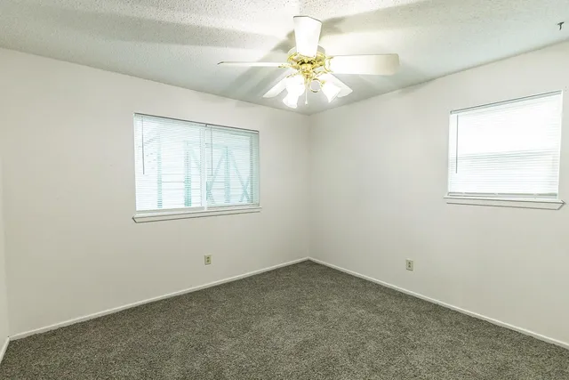 an empty room with a chandelier fan and windows