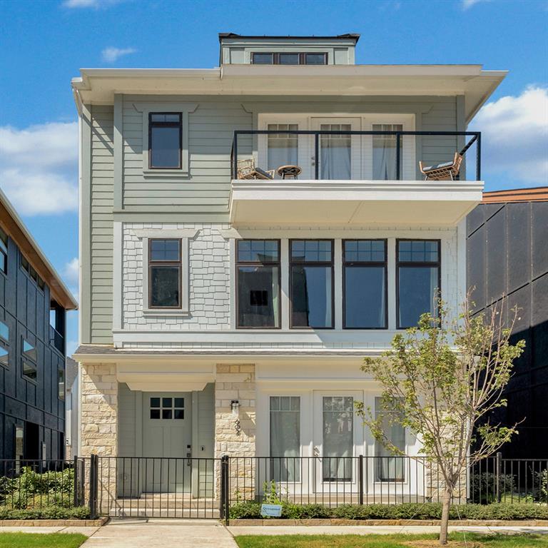 602 Winners Circle Rowlett, TX 75088 - Photo 2 of 35 Contemporary multi-story facade featuring light green siding, white shingle accents, stone veneer, a second-story balcony with metal railing, and a black metal fence enclosing the front yard