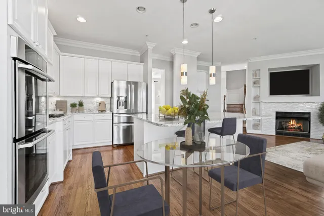 a kitchen with stainless steel appliances granite countertop a refrigerator a stove a sink a dining table and chairs with wooden floor