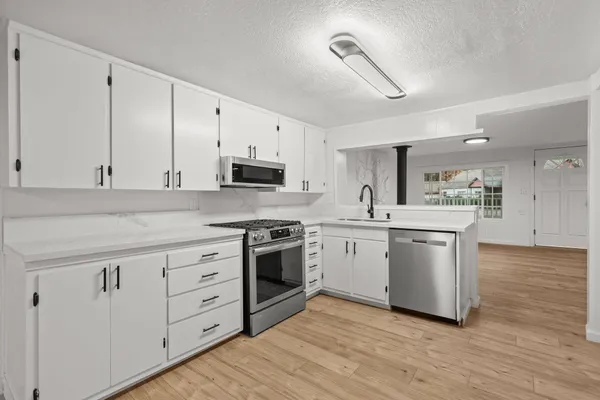 a kitchen with stainless steel appliances granite countertop a sink a stove a refrigerator and white cabinets