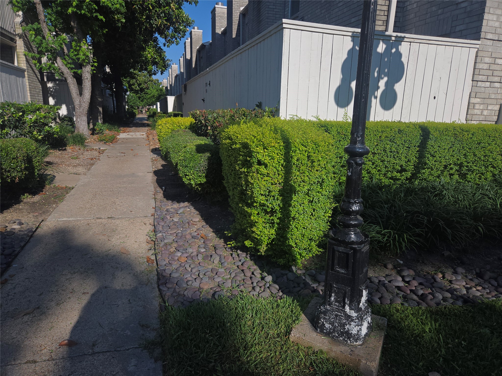 3780 Tanglewilde Street, Unit 501 Houston, TX 77063 - Photo 26 of 26 Charming walkway in a residential area with well-maintained hedges, a vintage-style lamp post, and a paved path lined with trees and stone accents, offering a peaceful and inviting atmosphere.