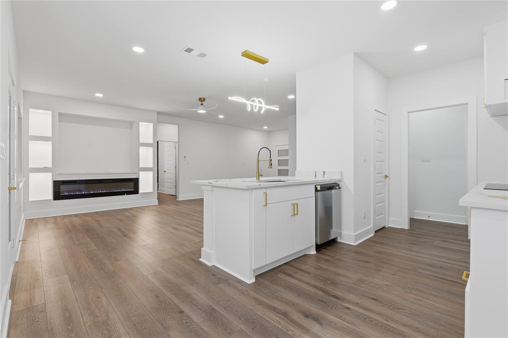 130 Cedar Elm Road Trinidad, TX 75163 - Photo 9 of 27 Open-concept living area featuring wood-finish flooring, a contemporary electric fireplace with built-in shelving, a kitchen island with a gold-tone faucet, white cabinetry with gold hardware, and a stainless steel dishwasher