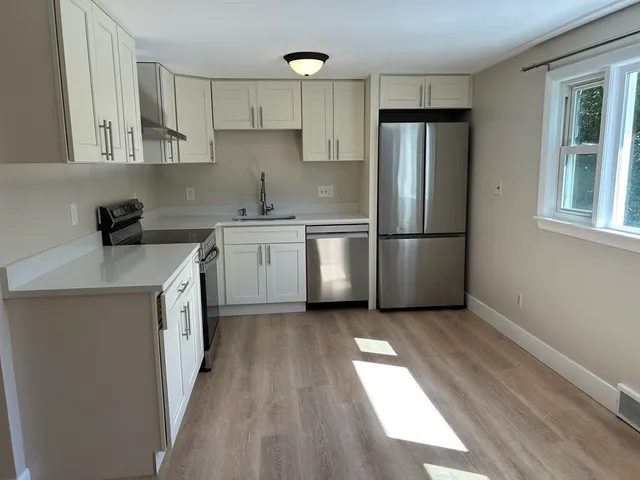 a kitchen with stainless steel appliances granite countertop a refrigerator a sink a stove and white cabinets