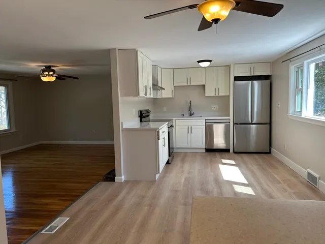 a kitchen with stainless steel appliances granite countertop a refrigerator a stove top oven a sink dishwasher and white cabinets with wooden floor