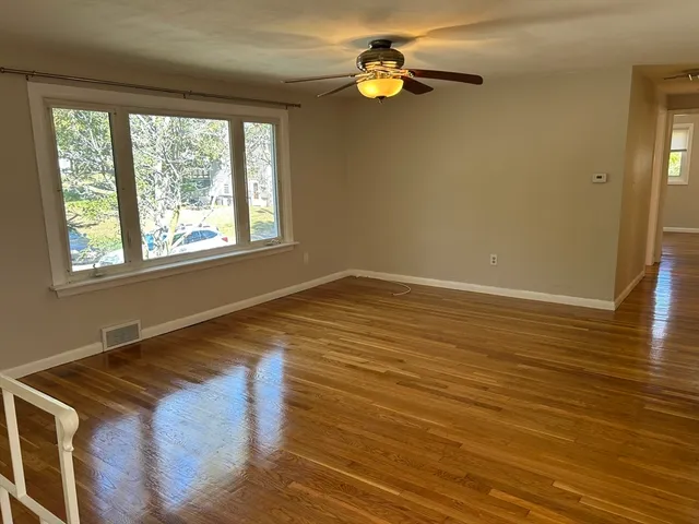 a view of empty room with wooden floor and fan
