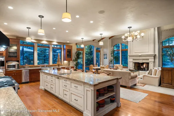 a kitchen with stainless steel appliances kitchen island granite countertop a stove a refrigerator a oven a dining table and chairs with wooden floor