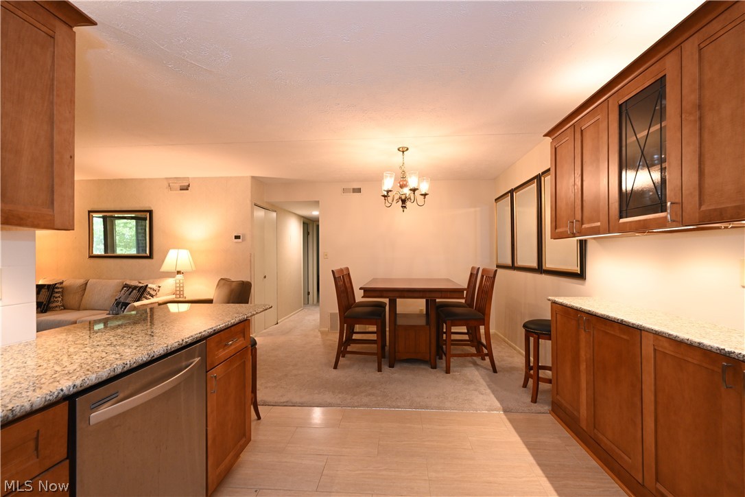 22962 Maple Ridge Road, Unit 108 North Olmsted, OH 44070 - Photo 10 of 37 Kitchen with a notable chandelier, dishwasher, light colored carpet, pendant lighting, and light stone countertops