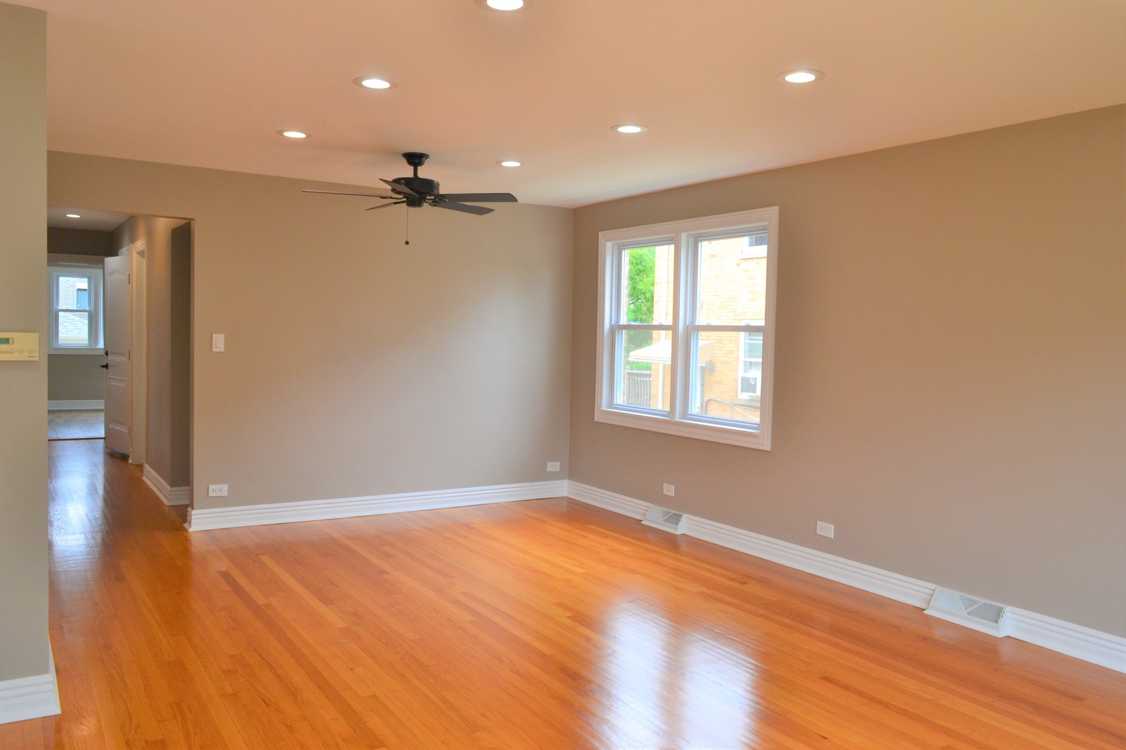 an empty room with wooden floor ceiling fan and windows