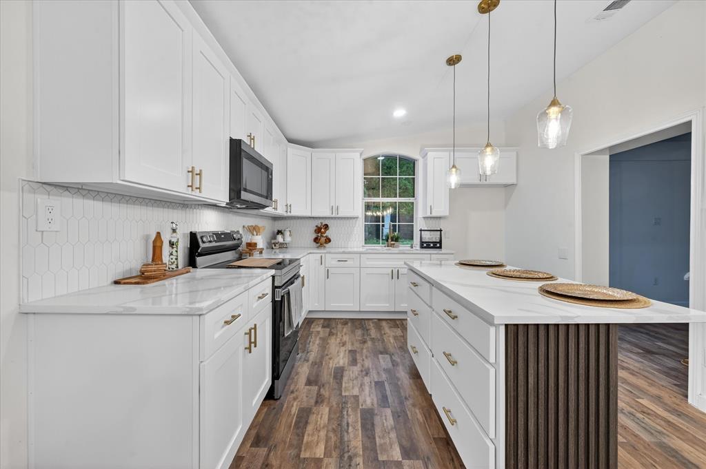 538 Pemberton Hill Road Dallas, TX 75217 - Photo 25 of 31 Modern kitchen featuring extensive white cabinetry, a large kitchen island with fluted paneling, wood-finish flooring, and pendant lighting
