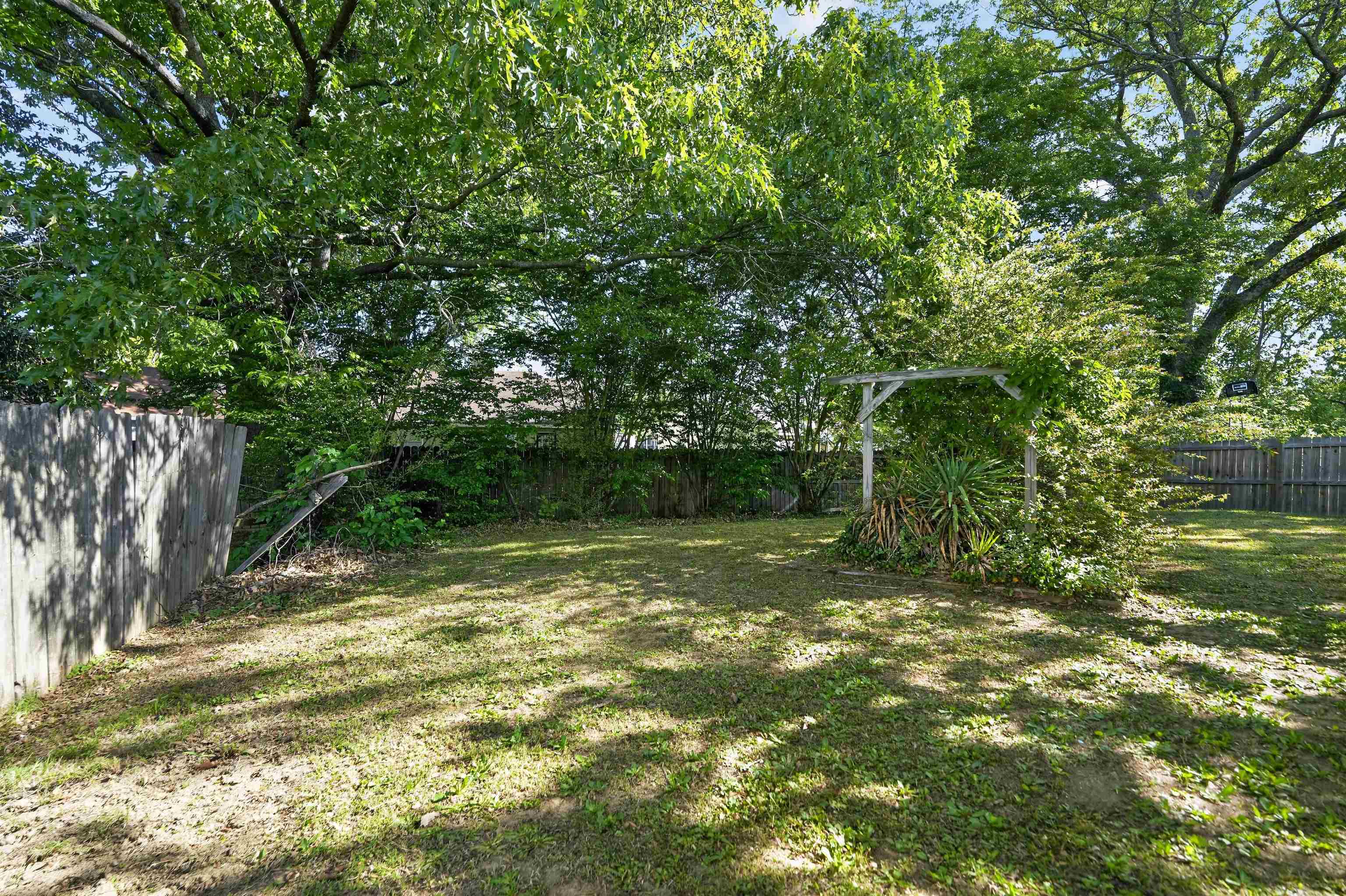 3372 Spring Shadow Drive Memphis, TN 38118 - Photo 4 of 35 Expansive backyard with a wooden fence boundary, mature trees providing shade, and a rustic wooden arbor feature