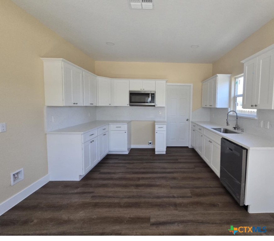 410 Trinity Street Luling, TX 78648 - Photo 4 of 10 a kitchen with wooden floors and white cabinets