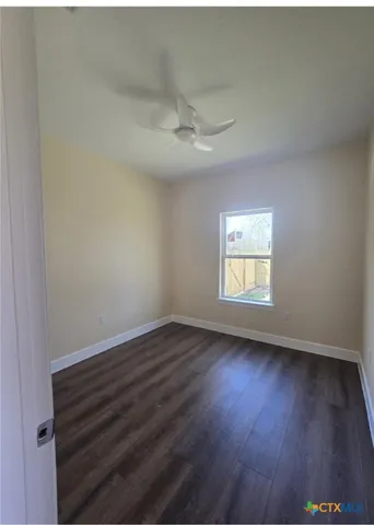 an empty room with wooden floor ceiling fan and window