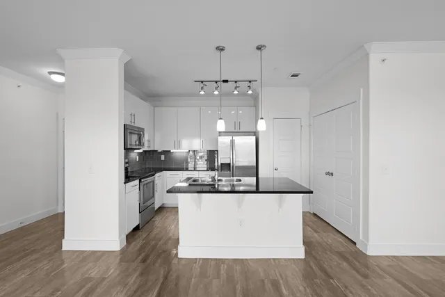 a large white kitchen with stainless steel appliances kitchen island a stove a refrigerator a sink dishwasher and white cabinets with wooden floor