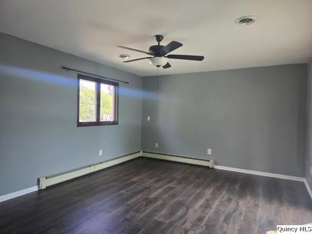 an empty room with wooden floor ceiling fan and windows
