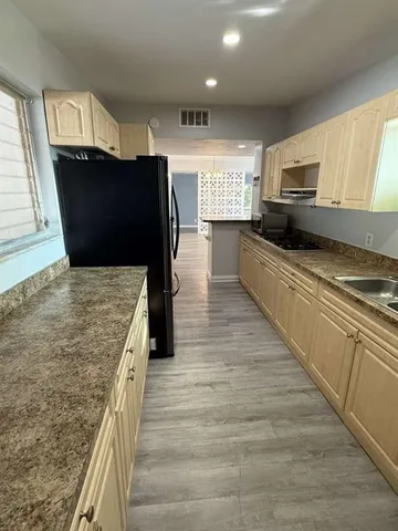 a kitchen with stainless steel appliances kitchen island granite countertop a refrigerator a stove and a sink with wooden floors