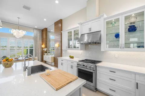 a dining room with kitchen island stainless steel appliances furniture a chandelier a large window and kitchen view