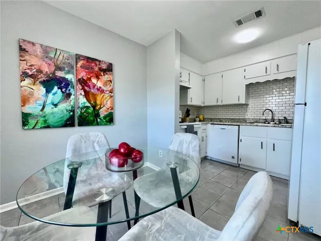a kitchen with stainless steel appliances kitchen island granite countertop a dining table chairs sink and cabinets