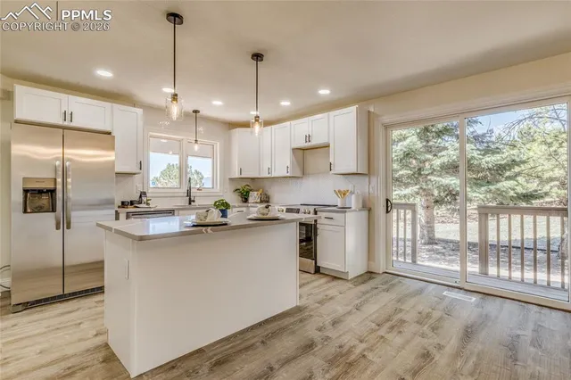 a kitchen with stainless steel appliances granite countertop a stove a sink a refrigerator and white cabinets with wooden floor